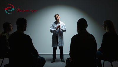 Темная комната, на врача направлен свет, пациенты в полутьме